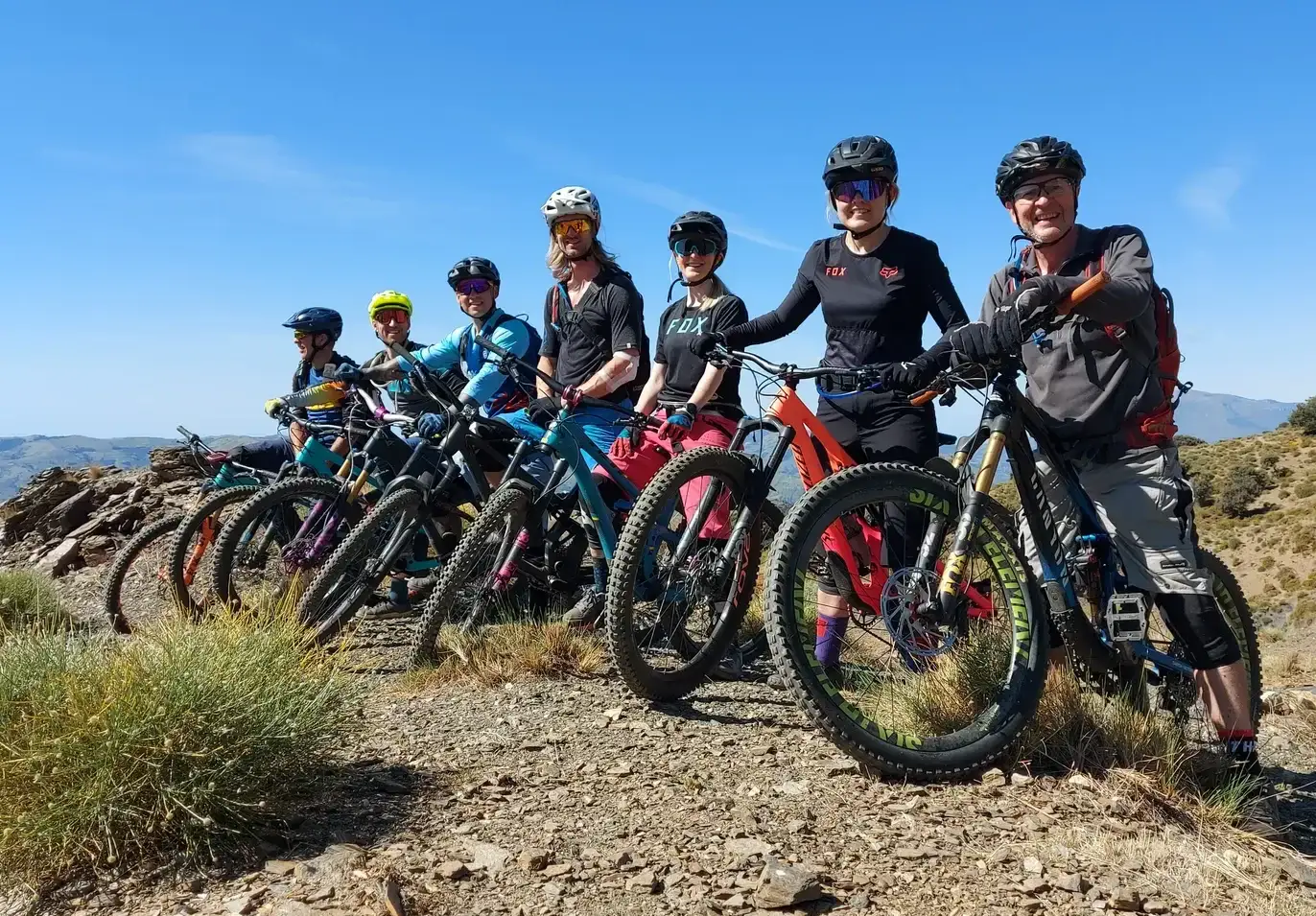 Group of 7 mountain bikers standing on a ridge with bikes